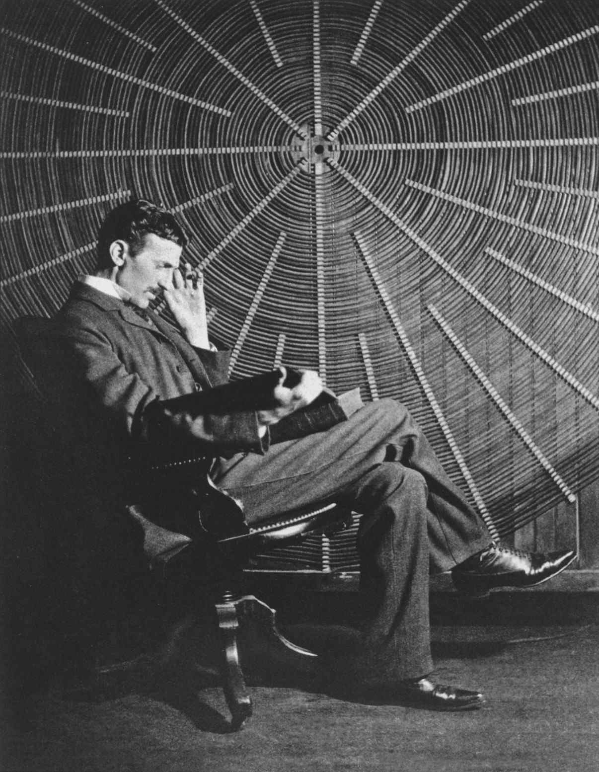 Tesla sitting in front of a spiral coil used in his wireless power experiments at his East Houston St. laboratory