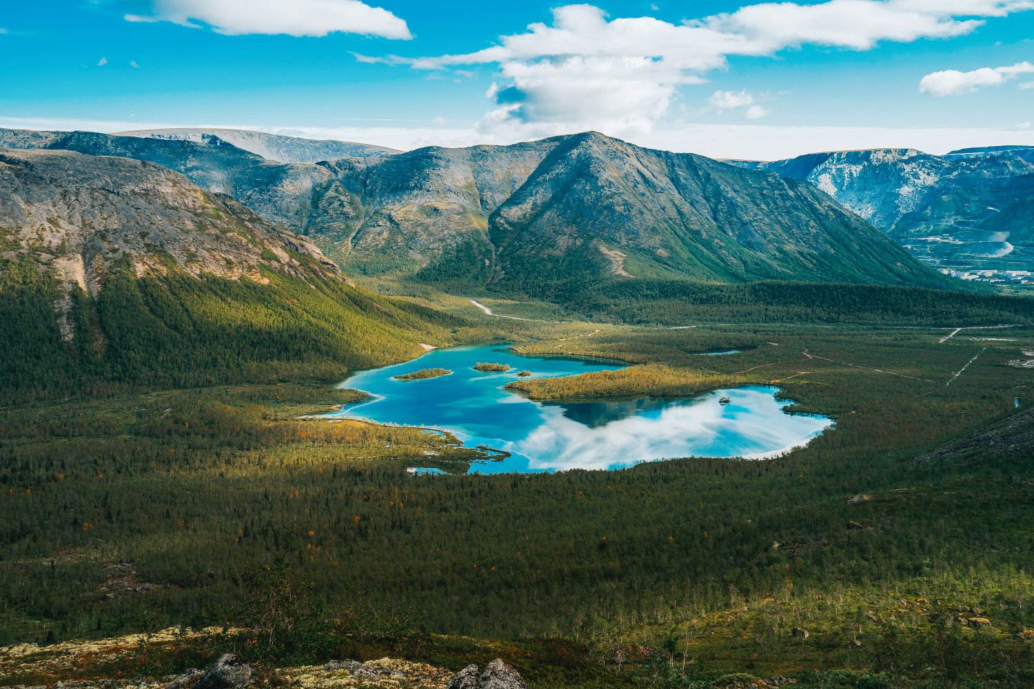 Beautiful blue lake with a reflection of the sky in valley on the background mountain picks in cloudy weather in polar summer, top view. Arctic, Kola Peninsula, Khibiny Mountains.