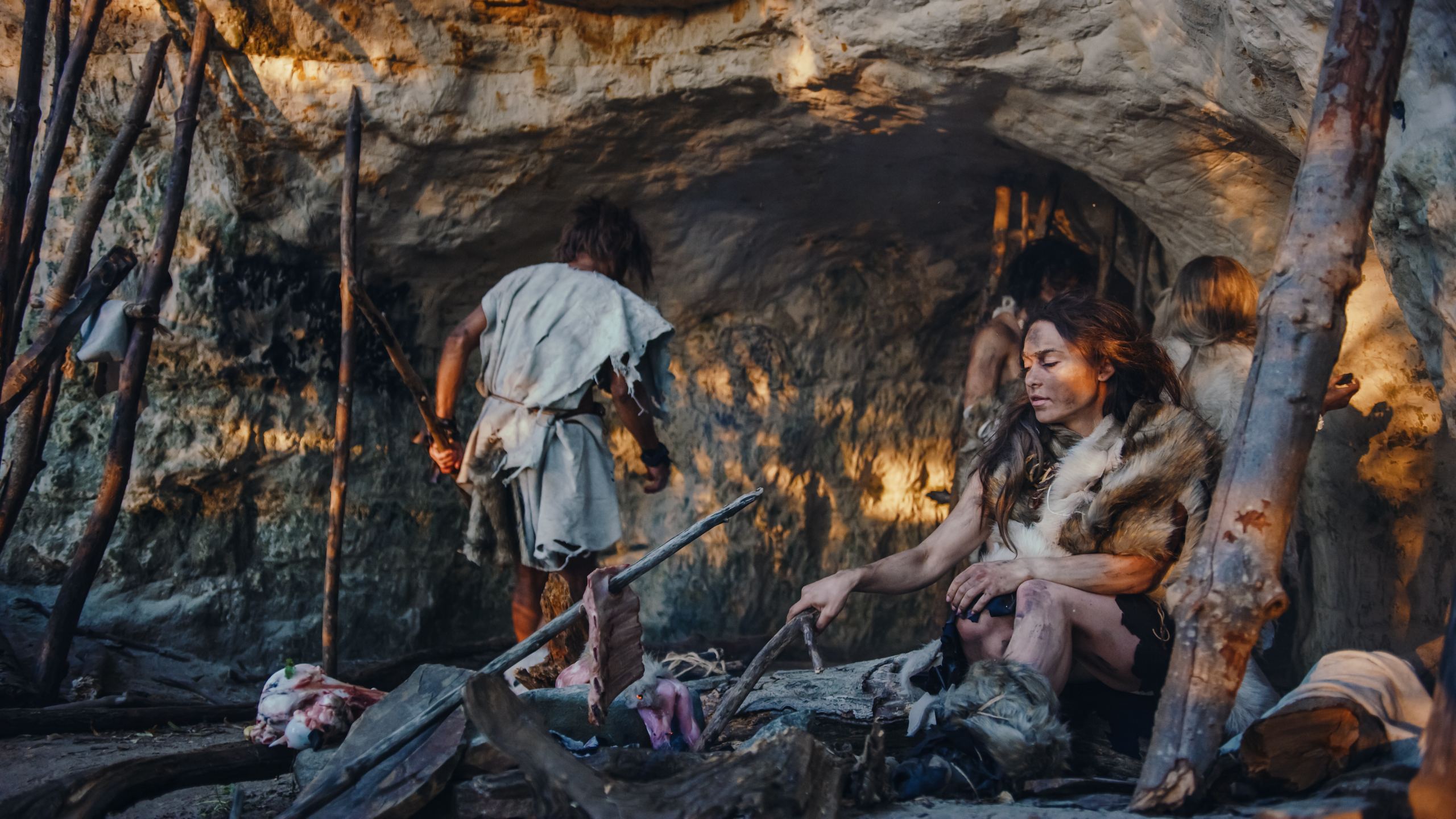 Una imagen recreativa de la familia neandertal Homo Sapiens. Tribu de cazadores-recolectores que visten pieles de animales viven en una cueva. Líder trae presas animales de la caza, una mujer cocina comida en una hoguera, una niña dibuja en Wals creando arte.